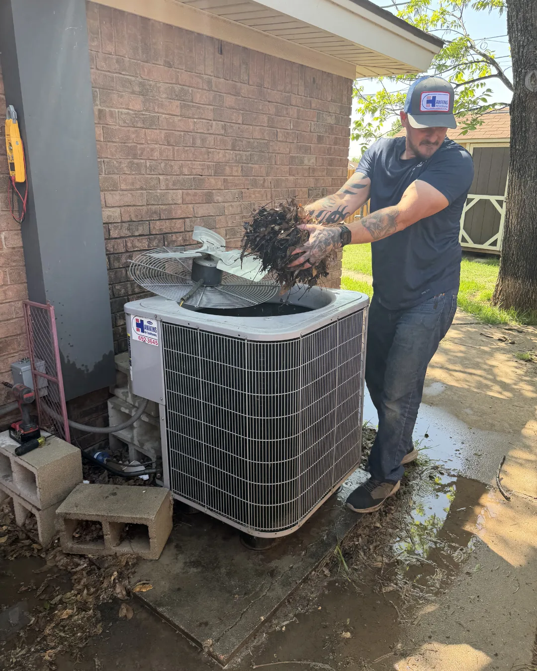 Hawkins technician clearing debris from an outdoor AC condenser in Abilene